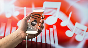 Modernes Online-Musik-Streaming-Konzept. Nahaufnahme eines Mannes hält Smartphone in der Hand und Musik hören mit mobilen App. Rot verschwommenen Notiz Hintergrund.